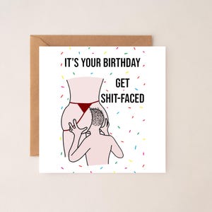 May include: A birthday card with a humorous illustration. The card features a cartoon image of a person's rear end with a thong, and another person's head. The text on the card reads, "IT'S YOUR BIRTHDAY GET SHIT-FACED."