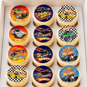 Puede incluir: Un conjunto de doce cupcakes dispuestos en una caja blanca, cada uno con una imagen comestible circular que muestra coches Hot Wheels, llamas, patrones de cuadros y el texto Happy Birthday. Los diseños incluyen varios coches y camiones.