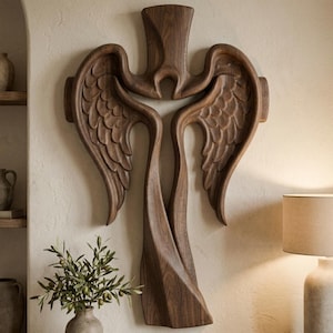 May include: A dark brown wooden wall sculpture featuring a stylized cross shape integrated with two large, detailed angel wings. The wood grain is visible throughout the piece, which has smooth, curved edges and a symmetrical, flowing design.