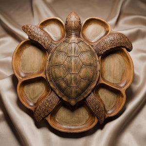 May include: A brown wooden serving tray shaped like a sea turtle with a central shell design and six surrounding recessed compartments for food. The turtle features detailed carved scales on its head and four flippers with a smooth finish.