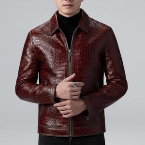 Puede incluir: Chaqueta de cuero burdeos con textura de piel de cocodrilo. La chaqueta tiene cierre de cremallera, cuello y ribete marrón oscuro. La persona lleva un cuello alto negro debajo.