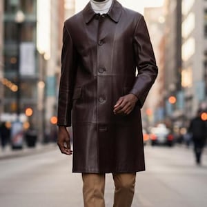 May include: A dark brown leather coat with a button-up front, worn over a white turtleneck and tan pants. The coat has a classic design and is knee-length. The person is wearing white sneakers.
