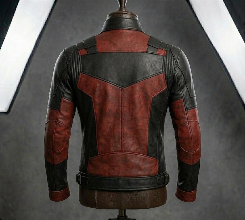 May include: A leather jacket with a two-tone design, featuring a combination of black and burgundy panels. The jacket has a classic biker style with a stand-up collar, shoulder accents, and a belt at the waist. The jacket is displayed on a mannequin.