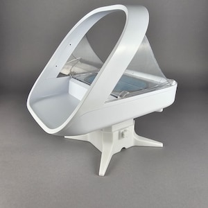 May include: A white, modern baby bassinet with a curved handle and a clear, protective canopy. The bassinet sits on a white, three-legged base, offering a clean and minimalist design.