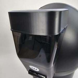 Może przedstawiać: Czarny system utylizacji odpadów po zwierzętach domowych z przezroczystym pojemnikiem i zakrzywioną, okrągłą podstawą. System posiada uchwyt i małą białą naklejkę z logo. Projekt jest nowoczesny i funkcjonalny.