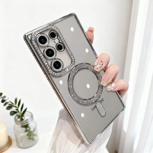 May include: Clear phone case with a silver glitter frame and a matching glitter ring. The case has a clear back with white polka dots and a silver glitter accent at the bottom. The phone case is for a Samsung phone.