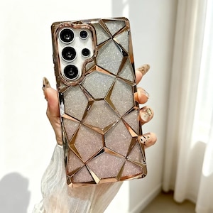 May include: A rose gold and silver geometric phone case. The case has a sparkling silver background with rose gold geometric shapes. The camera lenses are visible at the top. The case is held by a person.