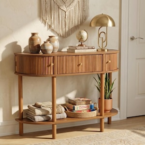 May include: A wooden console table with a curved front, featuring three drawers and a lower shelf. The table is adorned with decorative items, including vases, a globe, a lamp, and a potted plant. The table is made of light brown wood.