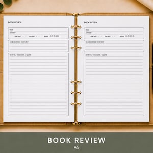 Peut inclure: Un agenda A5 ouvert avec des anneaux dorés présentant deux pages blanches avec des modèles de critique de livre imprimés en noir. Chaque page comprend des champs pour le titre, l'auteur, la date de début, la date de fin, la note et les avis.