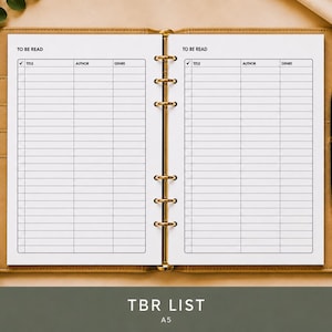 May include: An open A5 planner with a tan leather cover and gold-toned six-ring binder mechanism. The white pages feature a printed 'TO BE READ' list with columns for title, author, and genre. A black pen is tucked into the side of the planner.