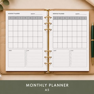 Könnte beinhalten: Ein offener A5-Monatsplaner mit hellbraunem Ledercover. Die Doppelseite zeigt ein Kalendarium, Notizen und To-Do-Bereiche. Ein grüner Stift liegt rechts. Der Text "MONTHLY PLANNER" und "A5" befindet sich unten.