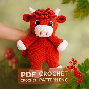 Puede incluir: Un peluche de toro rojo hecho a mano con detalles blancos en la cara, las pezuñas y los cuernos. El toro tiene grandes ojos negros y una melena roja y esponjosa. El texto "PDF CROCHET CROCHET PATTERN ENG" se muestra en un rectángulo marrón.