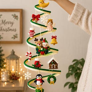 Puede incluir: Una decoración de árbol de Navidad de ganchillo en forma de espiral con una luna creciente amarilla en la parte superior y varios adornos colgantes, incluyendo un lazo rojo, un copo de nieve blanco, un ángel, un reno, un elfo, una campana amarilla, un bastón de caramelo, un calcetín, una casa, un pingüino, una corona y un regalo verde.