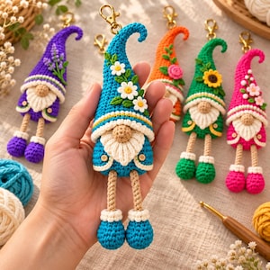 Puede incluir: Una colección de cinco llaveros de gnomos tejidos a ganchillo hechos a mano en colores vibrantes que incluyen azul, morado, naranja, verde y rosa. Cada gnomo presenta un sombrero puntiagudo decorado con flores, nariz redonda, barba blanca y piernas.