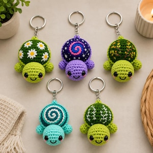 Peut inclure: Cinq porte-clés tortues en crochet avec des anneaux métalliques. Les tortues présentent divers motifs de carapace, notamment des marguerites blanches, une spirale violette, du feuillage vert, un tourbillon bleu sarcelle et des feuilles blanches.