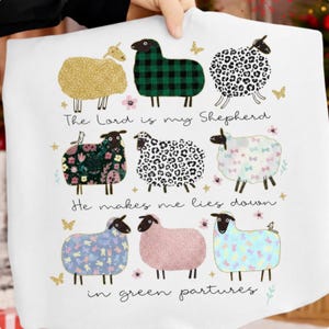 May include: White cushion cover with a design of nine sheep in different patterns and colours. The text reads "The Lord is my Shepherd, He makes me lies down in green pastures".