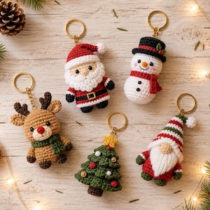 Puede incluir: Cinco llaveros de ganchillo con personajes navideños: un Santa Claus con traje rojo, un muñeco de nieve con sombrero negro y bufanda roja, un reno marrón con bufanda verde, un árbol de Navidad verde con estrella amarilla y un gnomo con gorro.