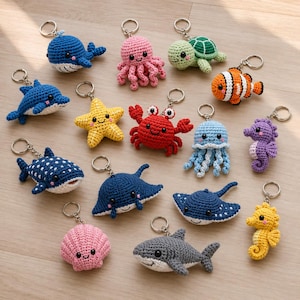 Può includere: Una collezione di quindici portachiavi all'uncinetto colorati raffiguranti varie creature marine, tra cui una balena blu, un polpo rosa, una tartaruga verde, un pesce pagliaccio arancione, un delfino blu, una stella marina gialla e un granchio rosso.