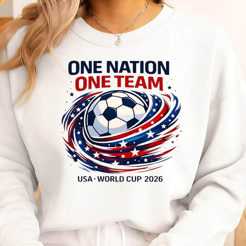 May include: White sweatshirt with a soccer ball graphic encircled by red, white, and blue swirls and stars. The text reads "ONE NATION ONE TEAM" and "USA WORLD CUP 2026".