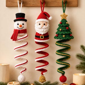May include: Three crocheted hanging ornaments featuring a snowman with a black hat and red scarf, a Santa Claus with a white beard and red suit, and a green Christmas tree with a yellow star, each ending in a long, spiraling, colorful tail.