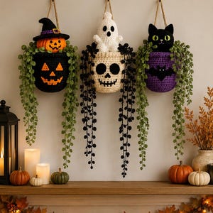 Op de afbeelding: Drie gehaakte wandmanden met Halloween-thema's. De linker mand is zwart met een pompoengezicht en een pompoen met een heksenhoed. Het midden is een schedel met een wit spookje. Rechts is een paarse mand met een zwarte kat.