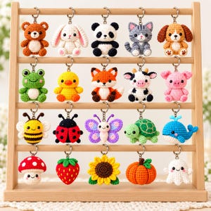 Può includere: Un espositore in legno contenente venti portachiavi all'uncinetto raffiguranti vari animali, insetti e piante. La collezione comprende un orso, coniglio, panda, gatto, cane, rana, pulcino, volpe, mucca, maiale, ape, coccinella, farfalla, tartaruga, balena, fungo, fragola, girasole, zucca e fantasma.