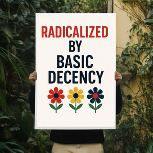 Peut inclure: Une affiche blanche avec le texte "RADICALIZED BY BASIC DECENCY" en rouge et bleu marine. En dessous, trois fleurs color&eacute;es : rouge, jaune et bleu marine. L'affiche est tenue devant un fond de verdure.