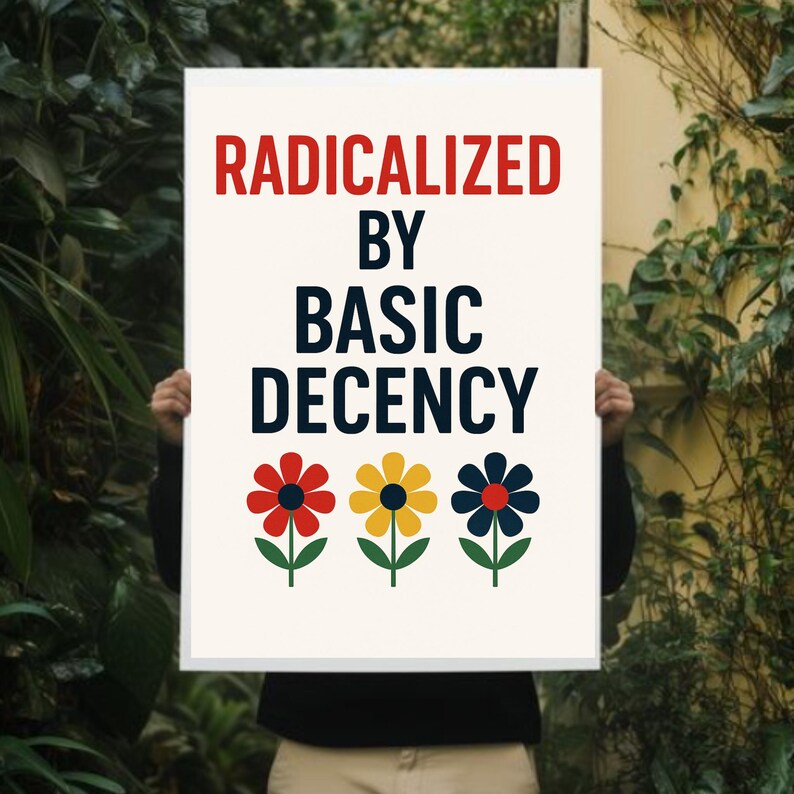 Peut inclure: Une affiche blanche avec le texte "RADICALIZED BY BASIC DECENCY" en rouge et bleu marine. En dessous, trois fleurs color&eacute;es : rouge, jaune et bleu marine. L'affiche est tenue devant un fond de verdure.