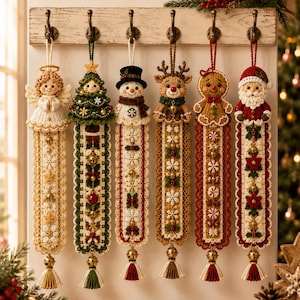 Peut inclure: Six décorations de Noël au crochet suspendues à un support en bois. Les personnages incluent un ange, un sapin, un bonhomme de neige, un renne, un bonhomme en pain d'épices et le Père Noël. Chaque figurine est fixée à une longue bande crochetée.