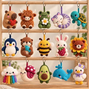 May include: A collection of fifteen crocheted animal and object keychains hanging on a wooden rack. The figures include a capybara with a heart, a highland cow, a frog with a flower, a sleeping cat, a turtle, a penguin, an otter, a bee, a rabbit with a strawberry, a sunflower bear, a rainbow cloud, a snail, an avocado, a whale, and a duck.