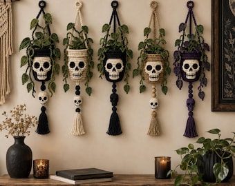 Puede incluir: Cinco maceteros de ganchillo para colgar en la pared, cada uno con un diseño de calavera en la maceta y un pequeño adorno de calavera sobre una borla. Los soportes contienen enredaderas verdes de ganchillo en colores negro, crema, negro, beige y morado.