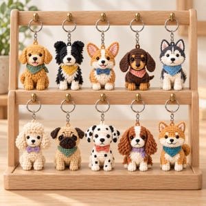May include: Ten crocheted dog keychains displayed on a two-tiered wooden stand. Each keychain features a different breed, including a golden retriever, border collie, corgi, dachshund, husky, poodle, pug, dalmatian, spaniel, and shiba inu, all wearing scarves or bow ties.