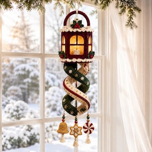 May include: A crocheted Christmas lantern ornament in deep red and cream, featuring a glowing light inside. Below the lantern hangs a spiraling, twisted fabric tail in dark green and cream with gold star embroidery, ending in three dangling charms.