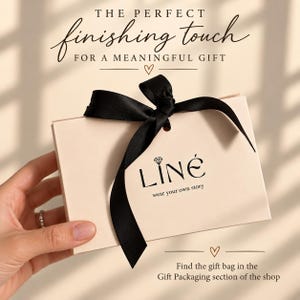 May include: A rectangular beige gift box tied with a black satin ribbon. The box features the black text LIN&Eacute;, a diamond icon, and the phrase wear your own story. Above the box is the text THE PERFECT finishing touch FOR A MEANINGFUL GIFT.