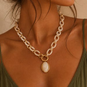 May include: A necklace featuring a thick chain of translucent off-white oval links interspersed with smaller gold-toned metal rings. A large, smooth, oval-shaped off-white stone pendant is suspended from the centre by a gold-toned metal ring.