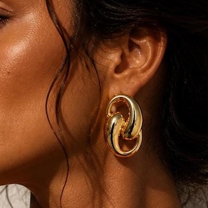 May include: A gold-toned earring featuring two interlocking, smooth, oval-shaped links. The earring has a polished, reflective surface with a rounded, chunky design that creates a continuous loop effect, hanging vertically from the earlobe.