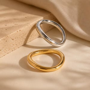 May include: Two smooth, rounded rings with a polished finish. One ring is silver-toned and the other is gold-toned. Both rings feature a continuous, slightly irregular circular shape with a thick, solid band design and a reflective surface.