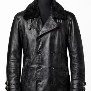 May include: A black leather coat with a double-breasted design and a faux fur collar. The coat features multiple buttons, two front pockets, and adjustable straps on the sleeves. The coat is displayed on a mannequin.