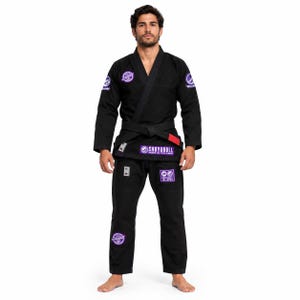 May include: A black Brazilian Jiu-Jitsu gi featuring a long-sleeve jacket and matching trousers. The uniform includes purple circular patches on the shoulders and leg, with a prominent purple Shoyoroll brand label on the jacket and a black belt.