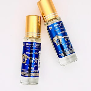 Può includere: Due bottiglie di profumo con tappi dorati ed etichette blu. Le etichette recitano "Have a Scent Collection" e "Smells Like Dylan Blue Pour Femme 12 ml." Le bottiglie sono trasparenti.