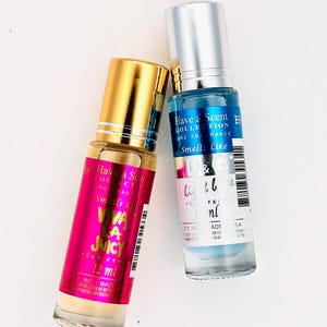 May include: Two perfume bottles. One has a gold cap and a pink label with the text "VIVA LA JUICY POUR FEM 12 ml". The other has a silver cap and a blue label with the text "light blue POUR FEM 12 ml".
