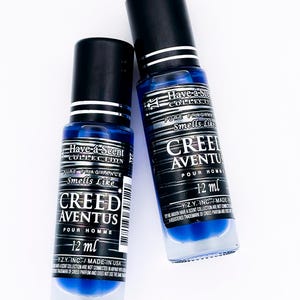 Puede incluir: Dos frascos de perfume de vidrio azul con tapas negras. Los frascos tienen etiquetas blancas con el texto "Have-a-Scent Collection", "Smells Like" y "Creed Aventus Pour Homme". Cada frasco contiene 12 ml de fragancia.