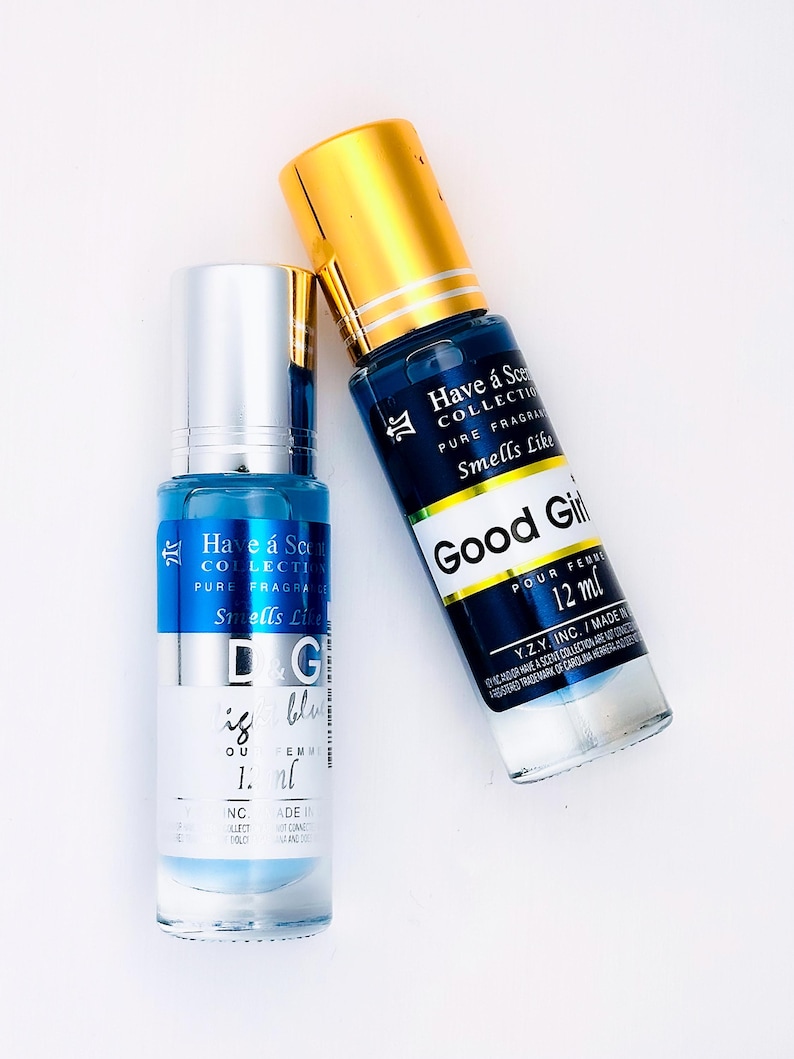 May include: Two perfume bottles with blue liquid and silver and gold caps are displayed on a white surface. One bottle has the text "D&G is blue" and the other says "Good Girl" and "12 ml". The bottles are from the "Have a Scent Collection".