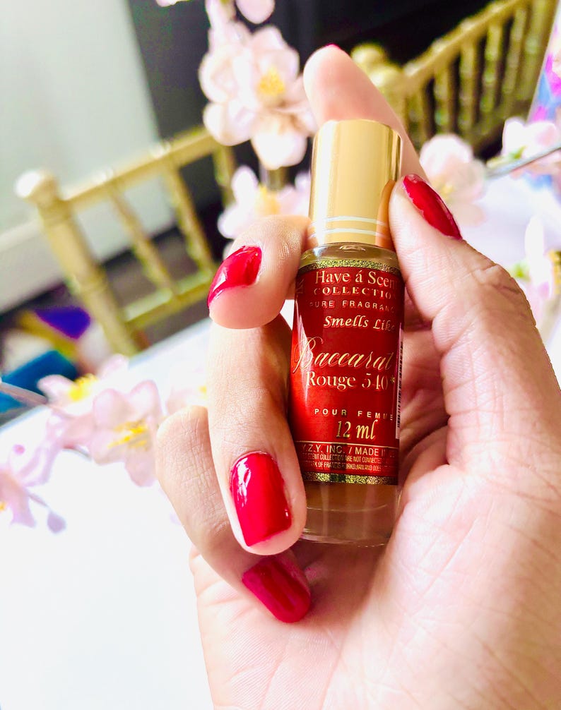 May include: A small perfume bottle with a gold cap and a red label is held in a hand with red nail polish. The label reads "Baccarat Rouge 540" and "12 ml". The bottle is part of the "Have a Scent Collection".