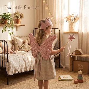 Puede incluir: Una niña pequeña con un conjunto de alas de mariposa rosas, una corona y una varita de estrella. El texto "The Little Princess" es visible en la esquina superior izquierda. La niña está en una habitación con una cama, juguetes y un banco de madera.