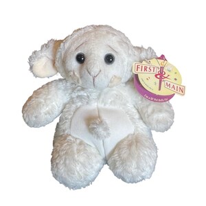 May include: A white plush lamb stuffed animal with black eyes and a stitched face. The lamb has a tag that reads "FIRST & MAIN" and "I'm a lil' Pot Belly Pal."