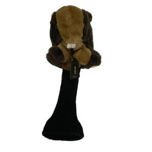 May include: A plush beaver golf club head cover featuring brown and tan fur, white teeth, and a black knit neck. A black rectangular tag hangs from the front, displaying the number 1 in gold print along with the brand name Wilson below it.
