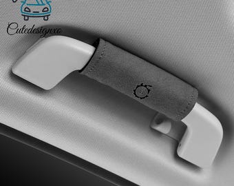 Può includere: Una copertura per maniglia di sostegno auto grigio chiaro con un manicotto in tessuto grigio scuro e un piccolo logo nero a forma di ingranaggio. La copertura avvolge una maniglia in plastica bianca. Il testo Cutedesignxo è visibile in alto.