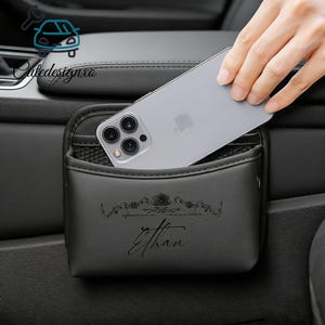 May include: Black car organizer with a pocket and a phone inside. The organizer has the name "Ethan" printed on it. The organizer is designed to fit in a car.