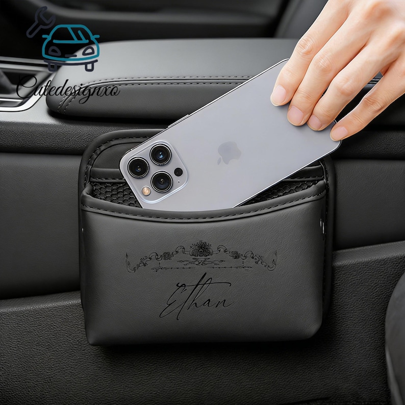 May include: Black car organizer with a pocket and a phone inside. The organizer has the name "Ethan" printed on it. The organizer is designed to fit in a car.